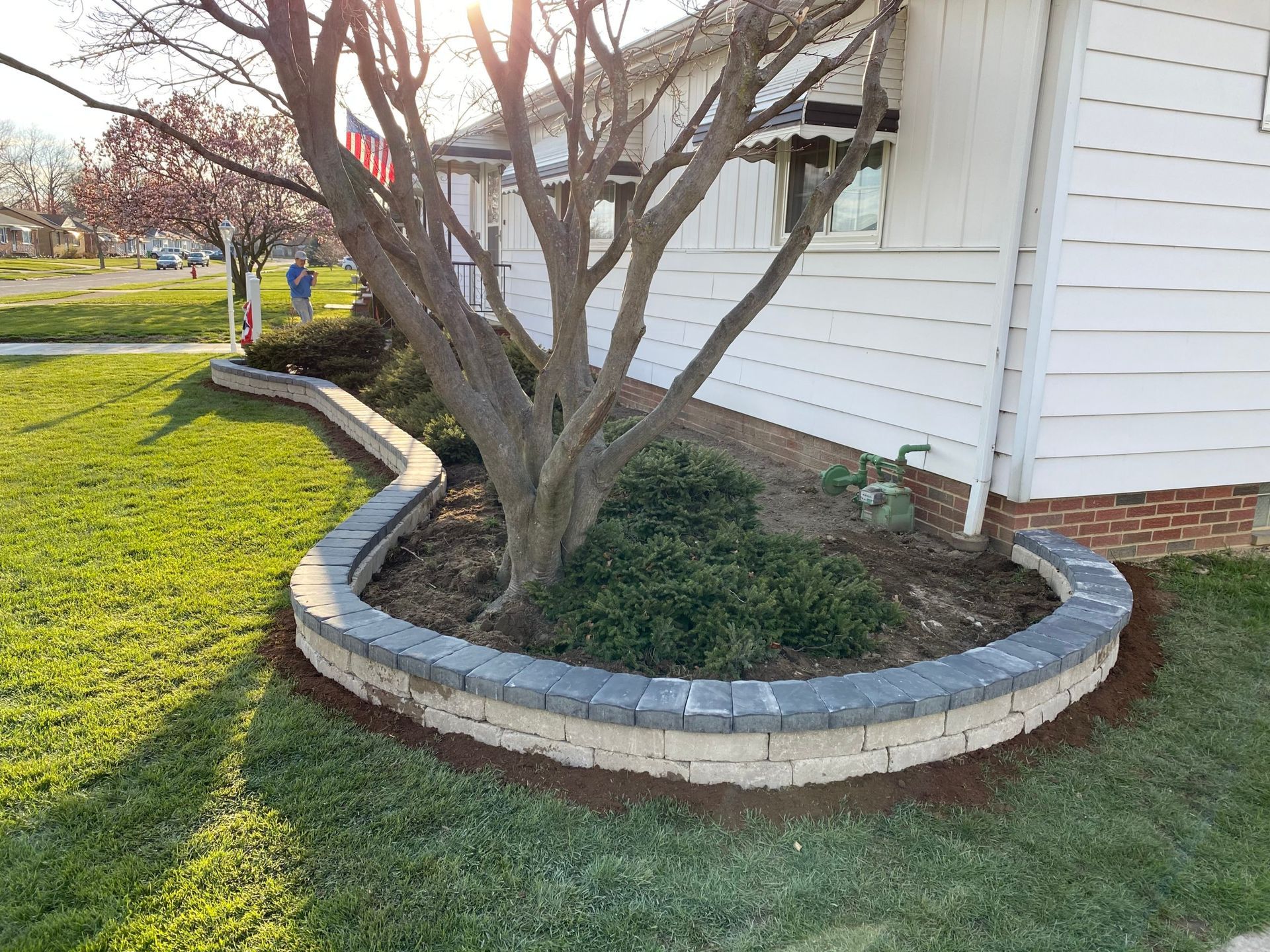 A white house with a tree in front of it and a brick border around it.