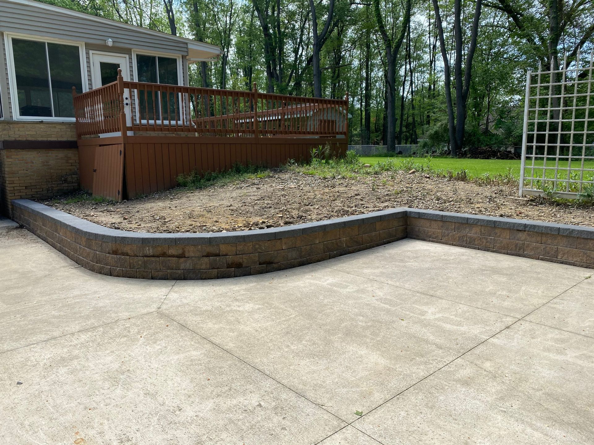 A patio with a wooden deck and a brick wall in front of a house.