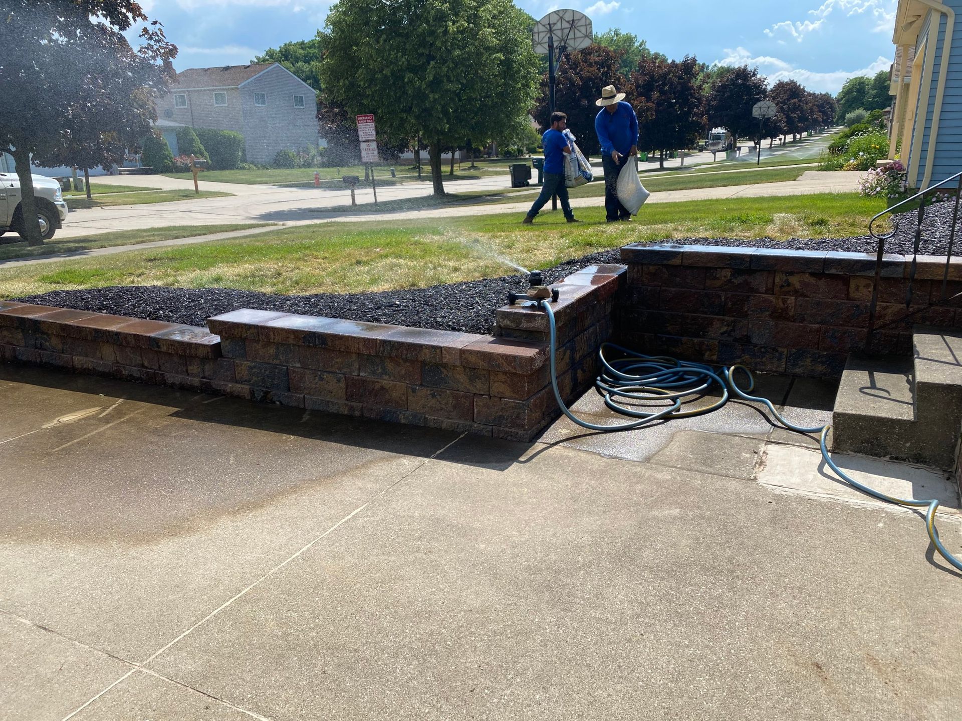 A couple of men are walking down a sidewalk next to a stone wall.