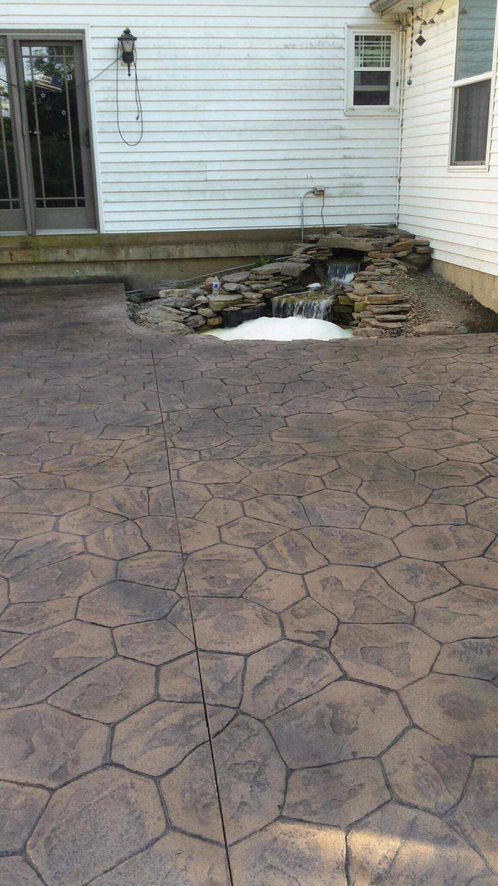 A patio with a waterfall in the background and a white house in the background.