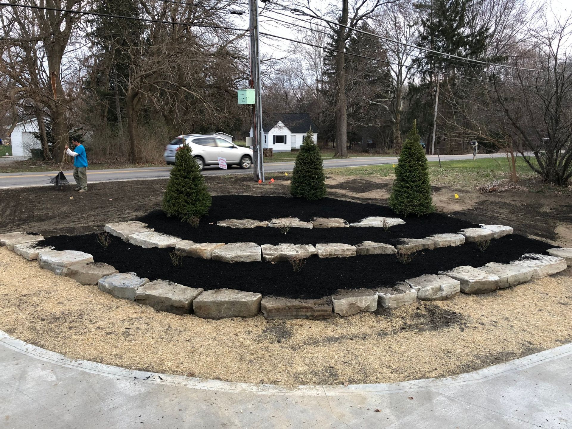 A man is standing in front of a garden with a car parked in the background.