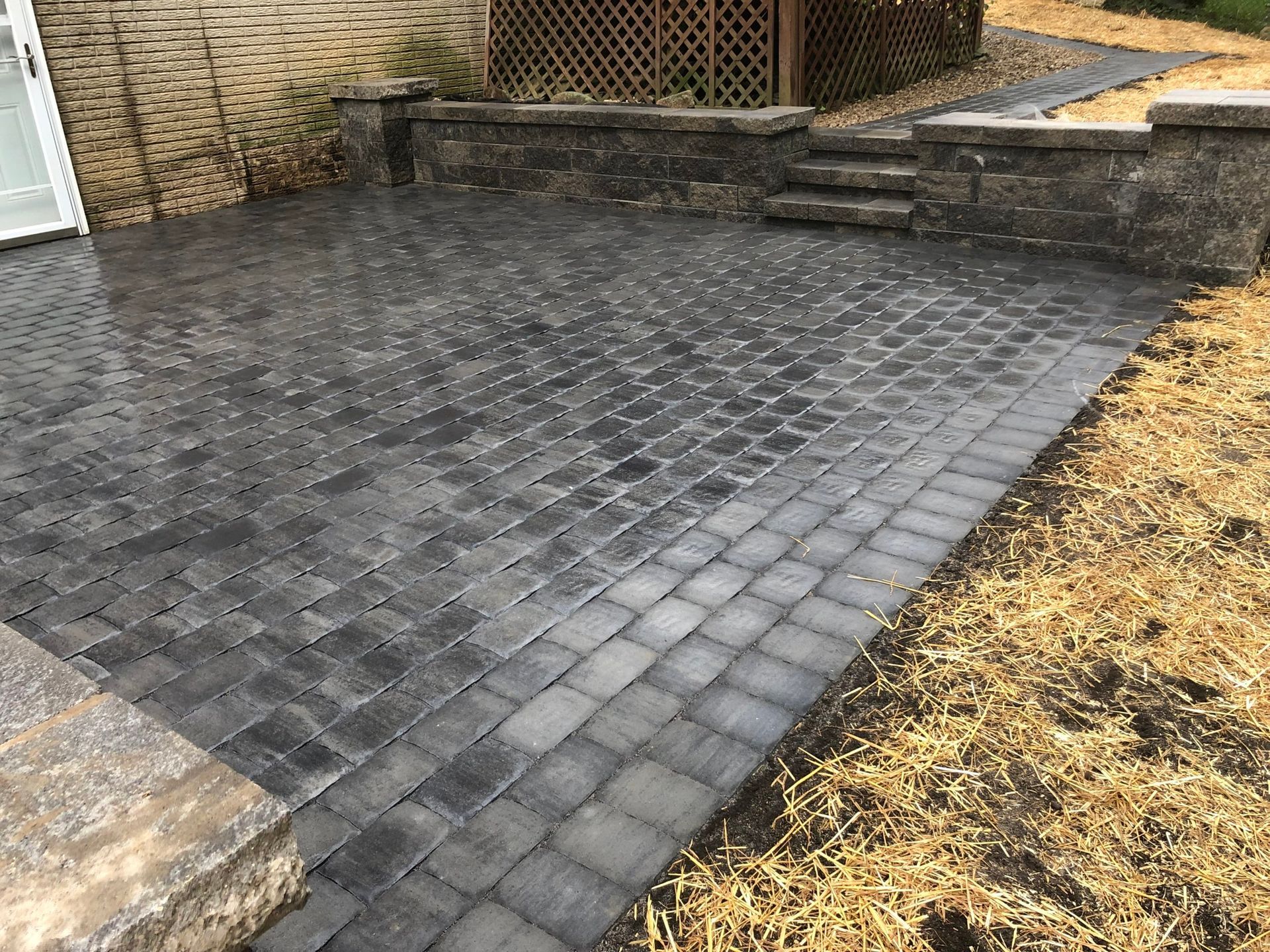 A brick patio with a stone wall and stairs in front of a house.