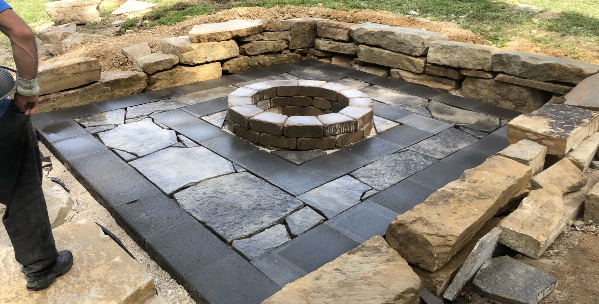 A man is standing next to a fire pit surrounded by rocks.