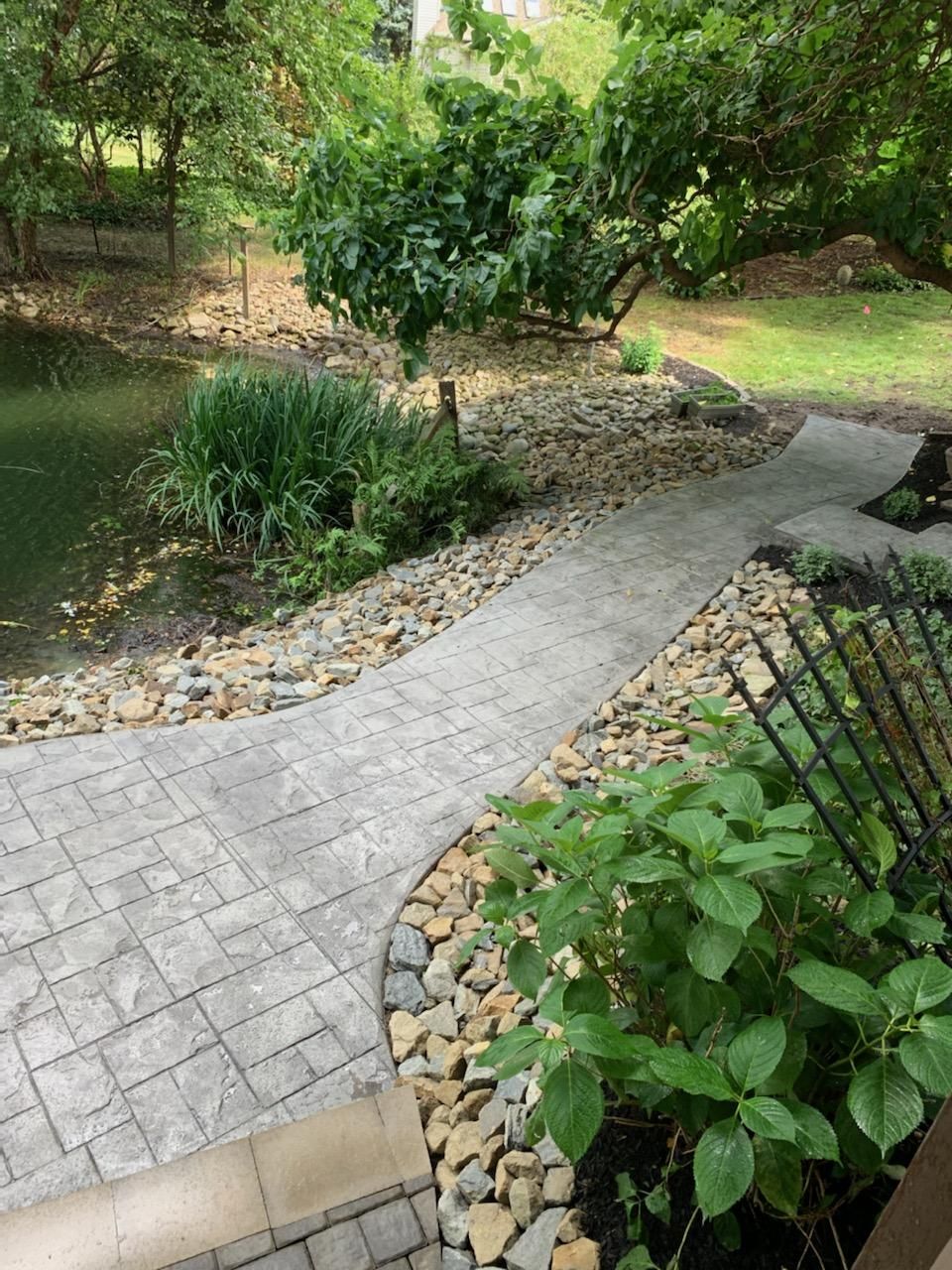 A brick walkway leading to a pond in a garden.