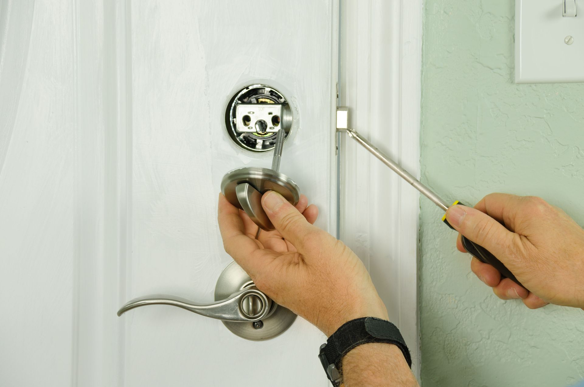 Person is installing a door handle on a white door with a screwdriver.