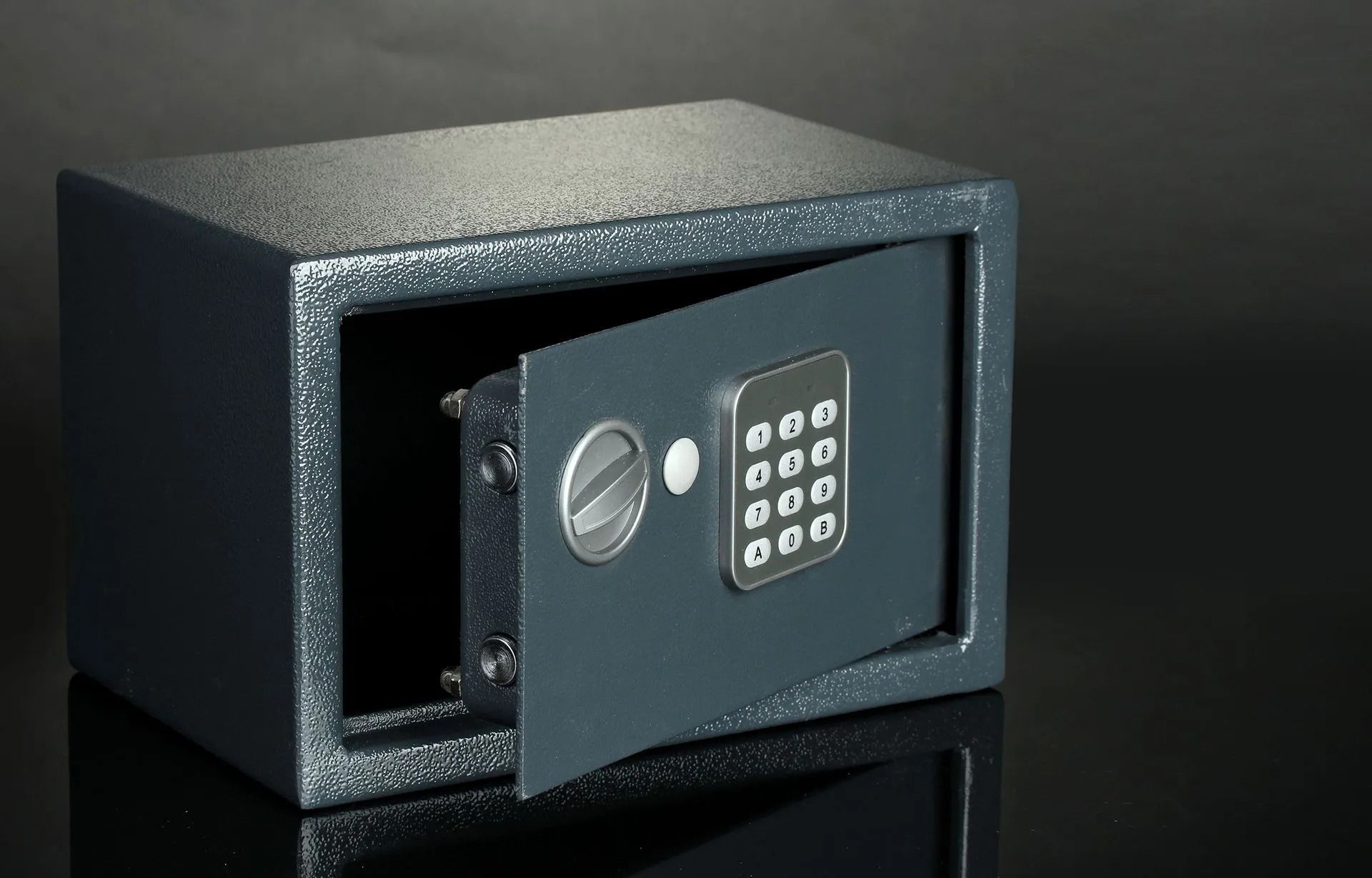 Opened dark gray safe with a digital keypad on a reflective black surface.