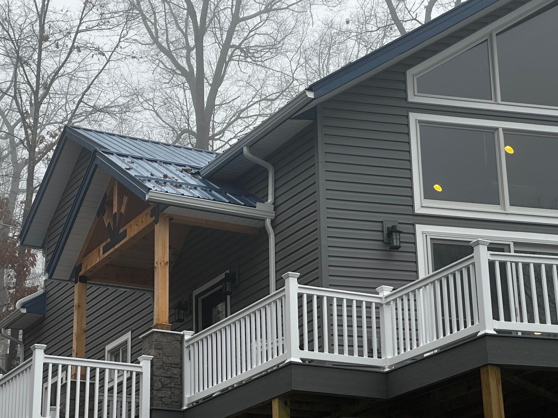 Gray house with blue metal roof, white railing, and wooden porch, in a misty setting.