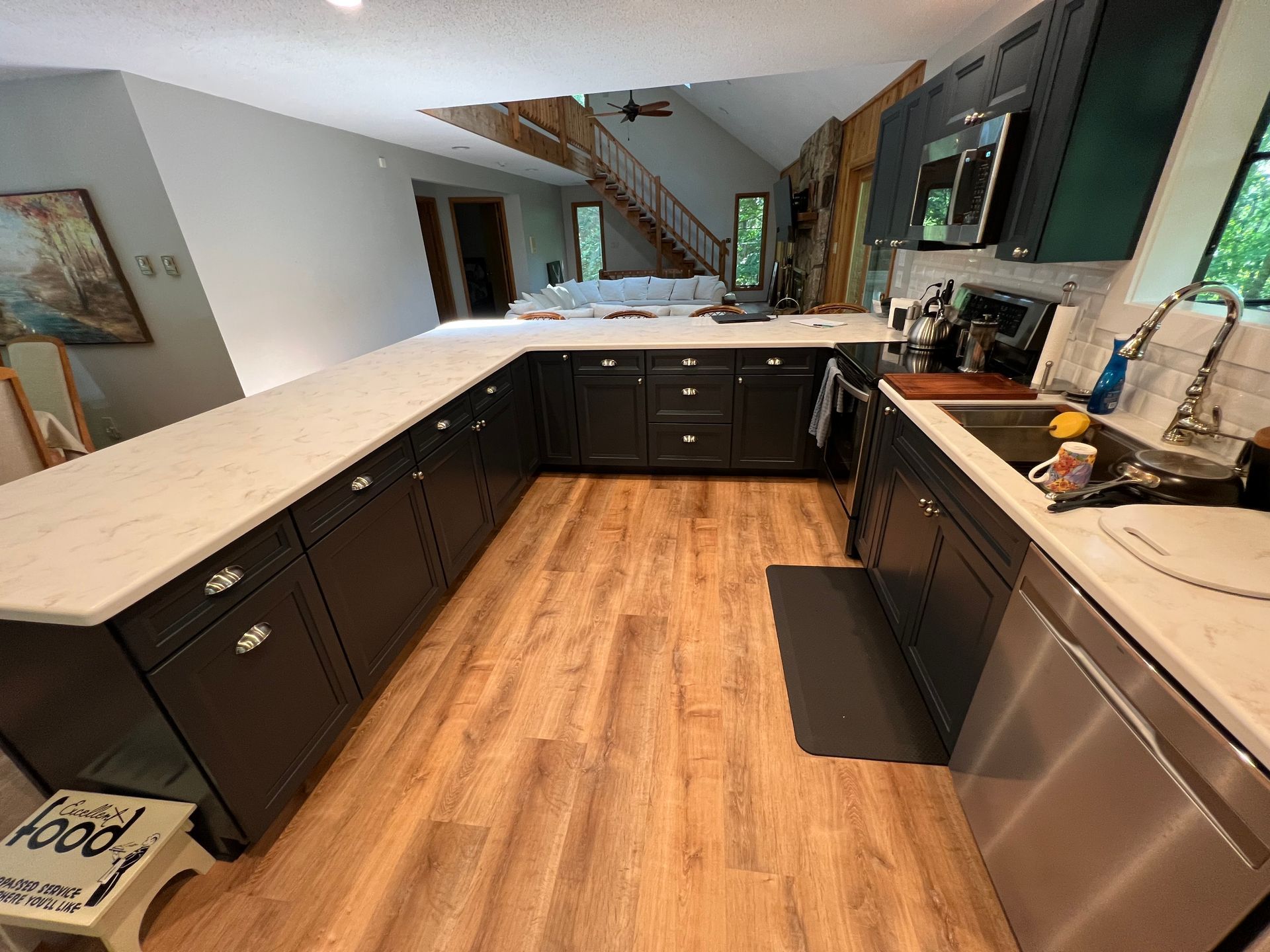 Dark gray kitchen with white countertops and wooden floor. A stainless steel dishwasher is visible.