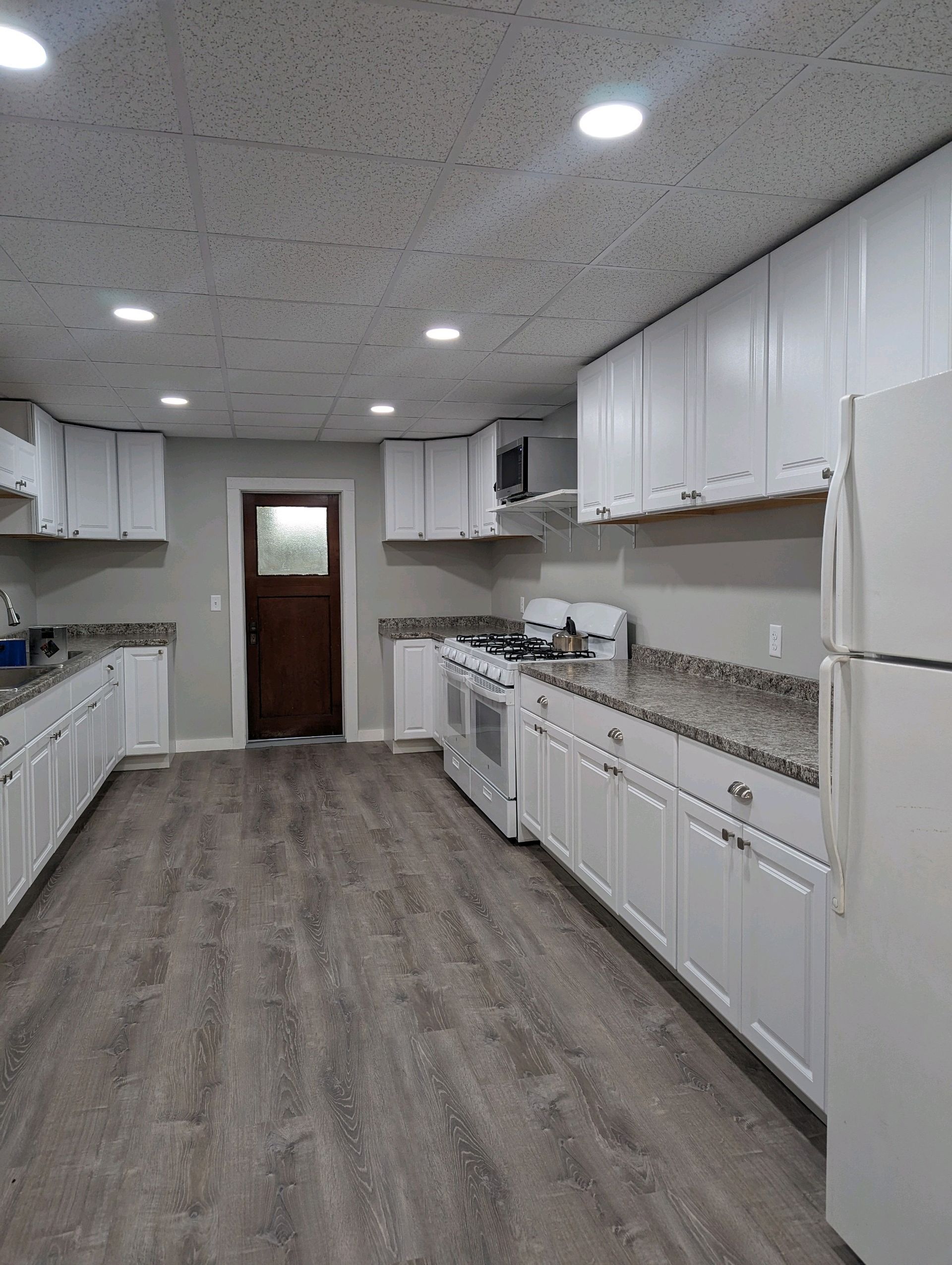 White kitchen with gray countertops and flooring, door in the background.