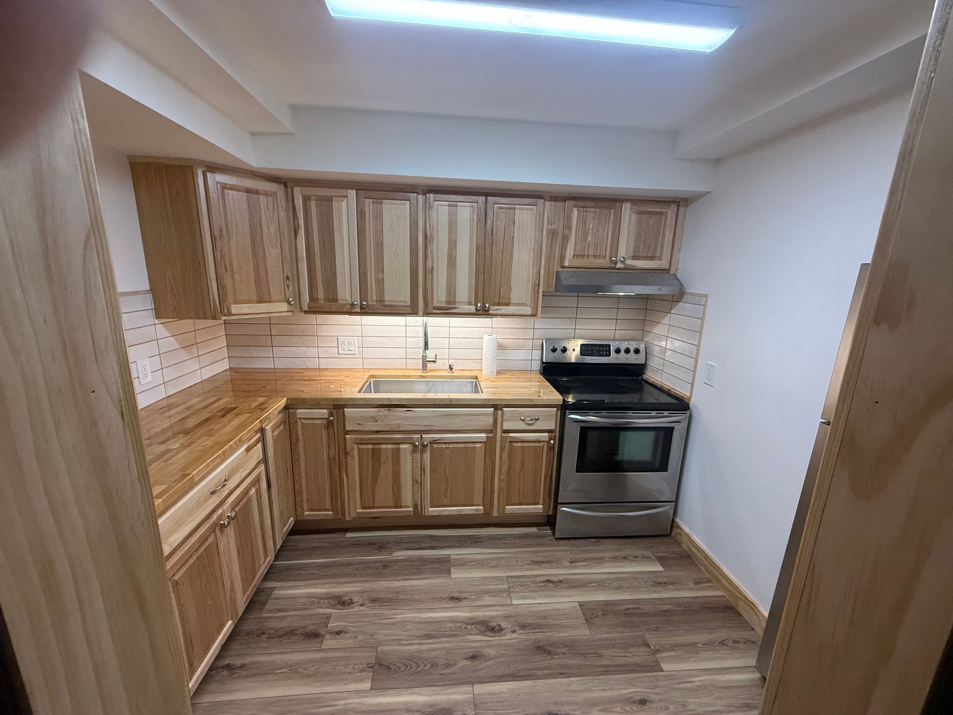Small kitchen with light wood cabinets, stainless steel appliances, and wood-look flooring.