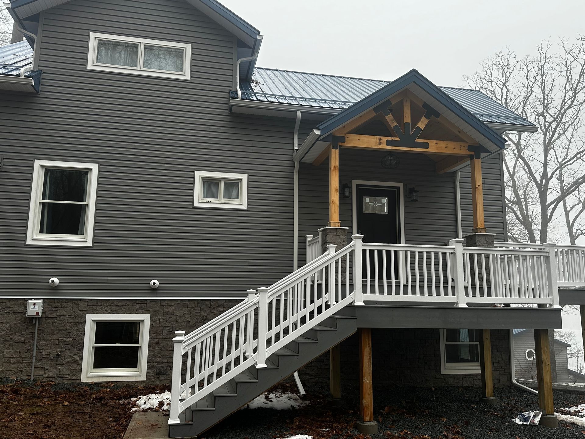 Two-story gray house with white deck and stairs leading to a covered porch.