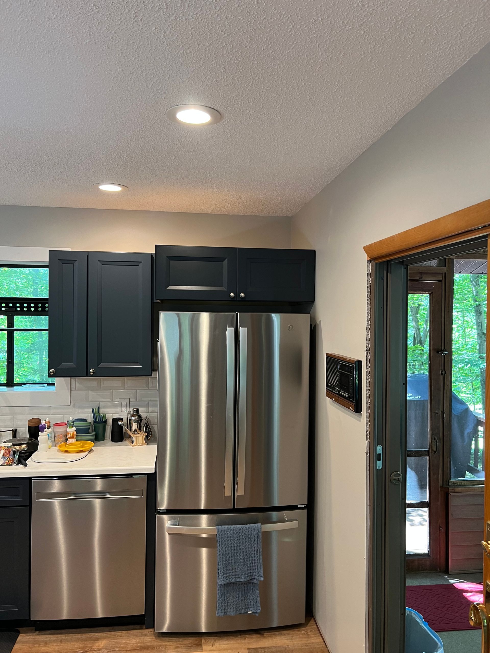 Kitchen with stainless steel refrigerator and dark blue cabinets. Gray walls and a sliding glass door.