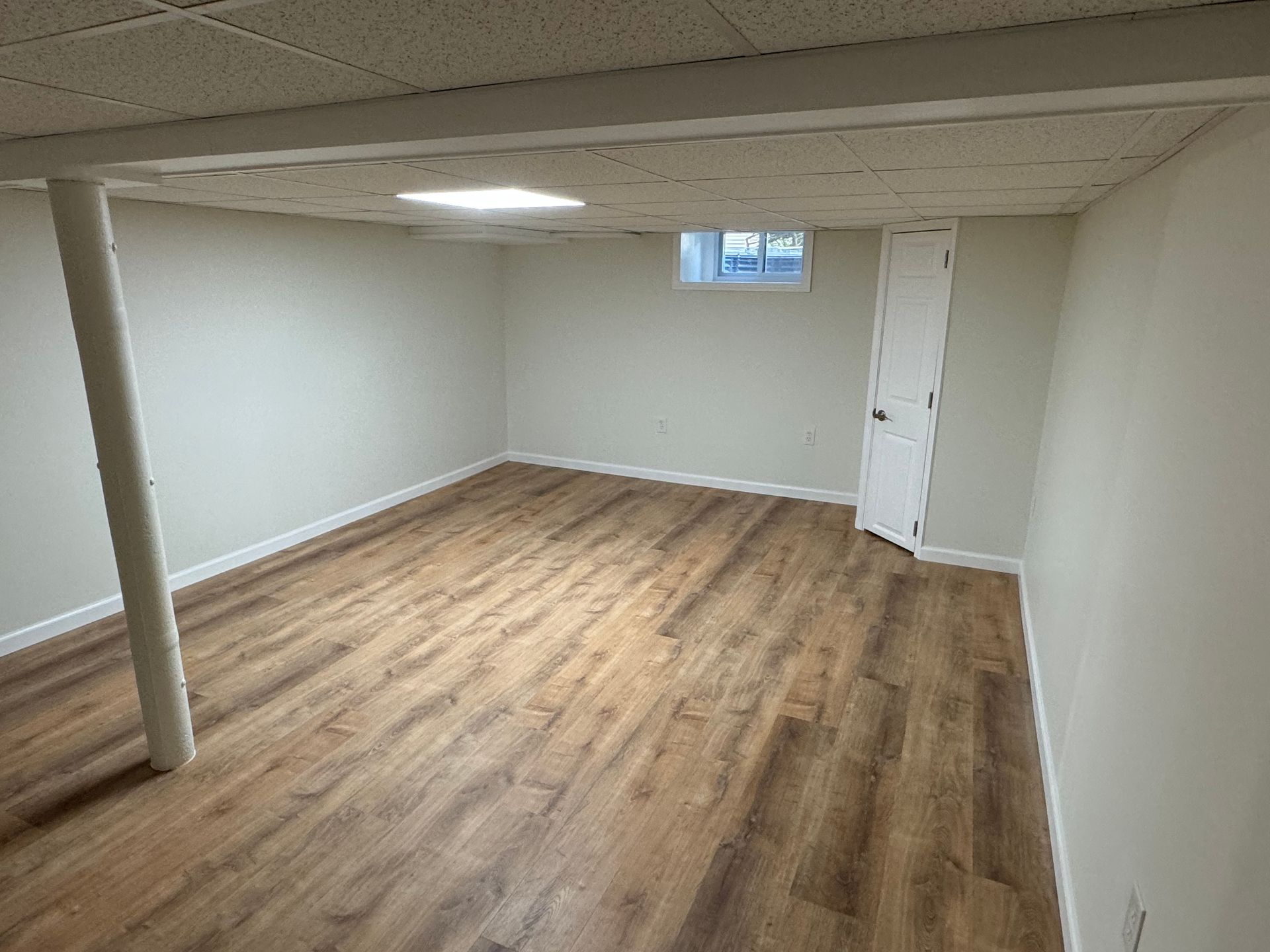 Empty room with wood-look flooring, white walls, and a support beam. A door and window are also present.