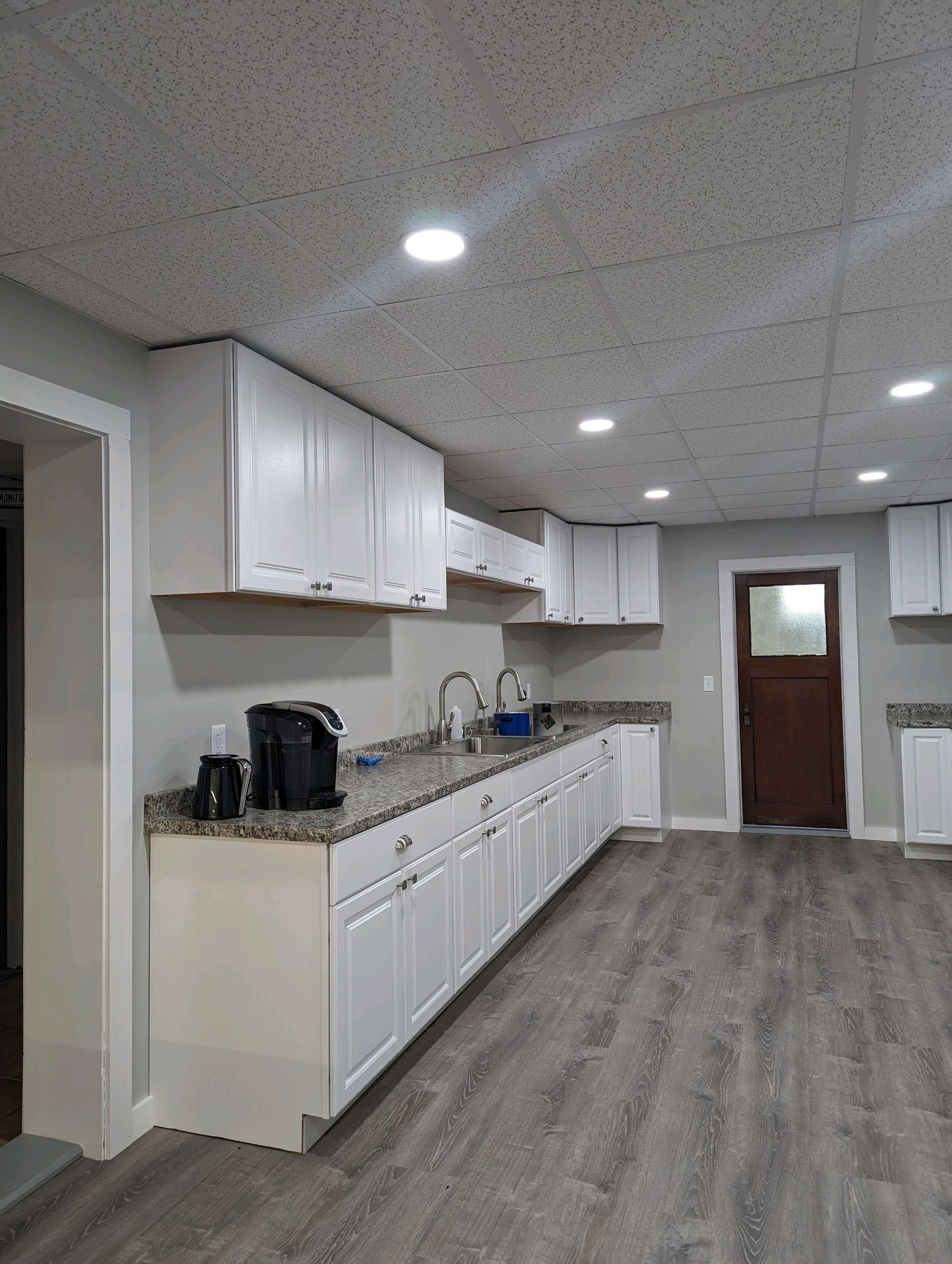 A newly renovated kitchen with white cabinets, gray countertops, and wood-look flooring.