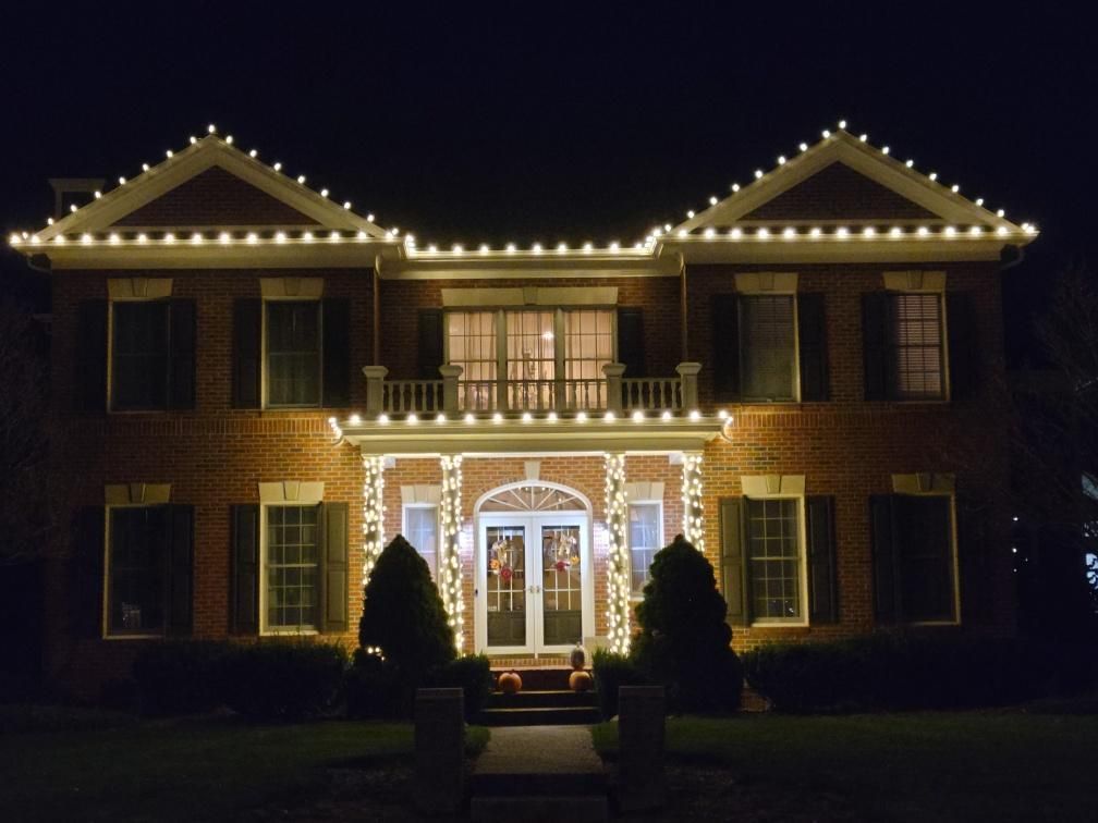 Brick house lit with warm white holiday lights at night, centered front entrance, dark sky background