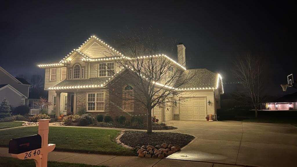 House at night decorated with warm white holiday lights, seen from the street and driveway