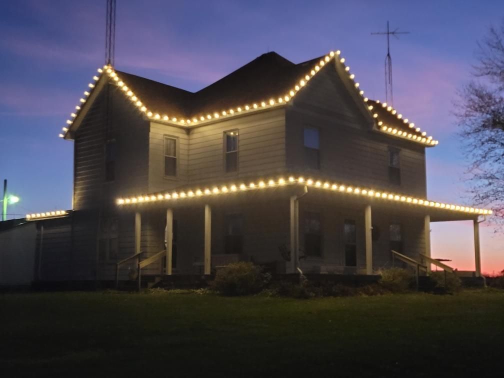 House outlined with warm string lights at dusk against a purple sky