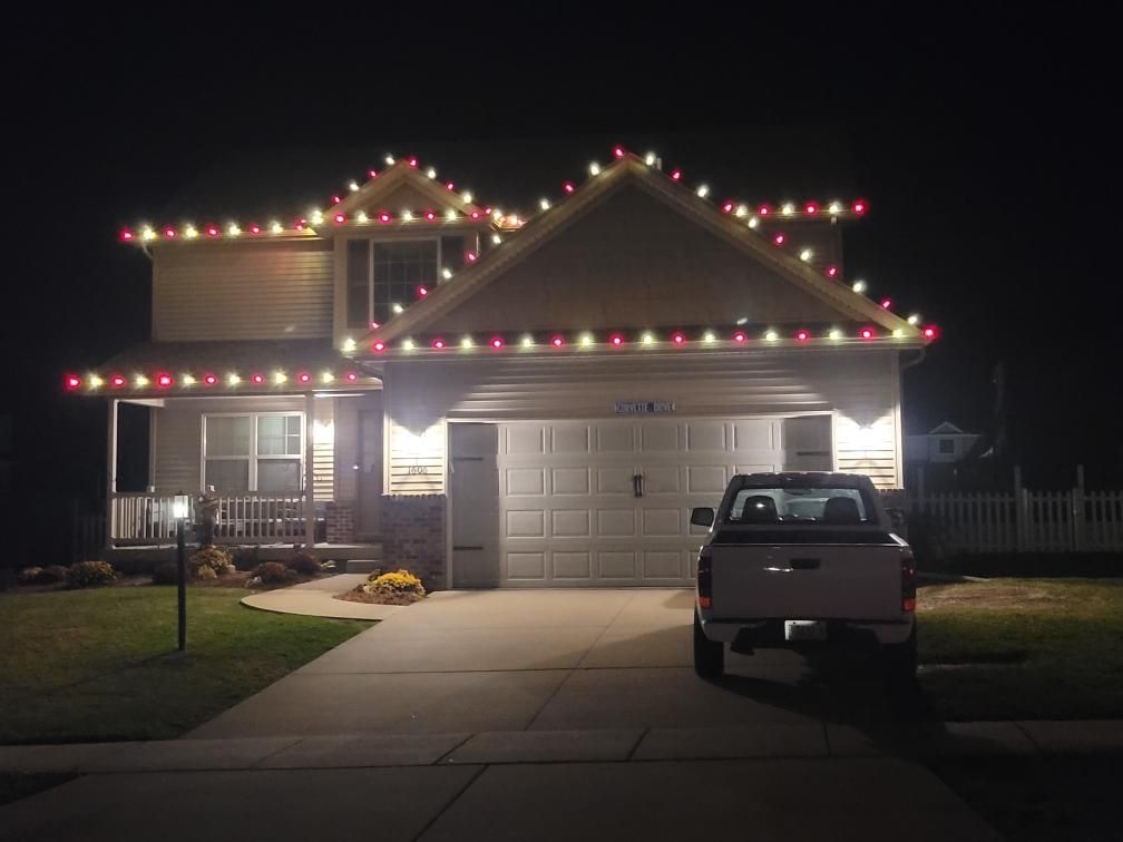 House decorated with red and green Christmas lights at night, with a pickup truck in the driveway.