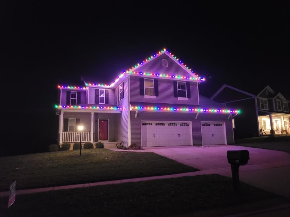 Suburban house at night outlined in purple and white holiday lights with two garage doors