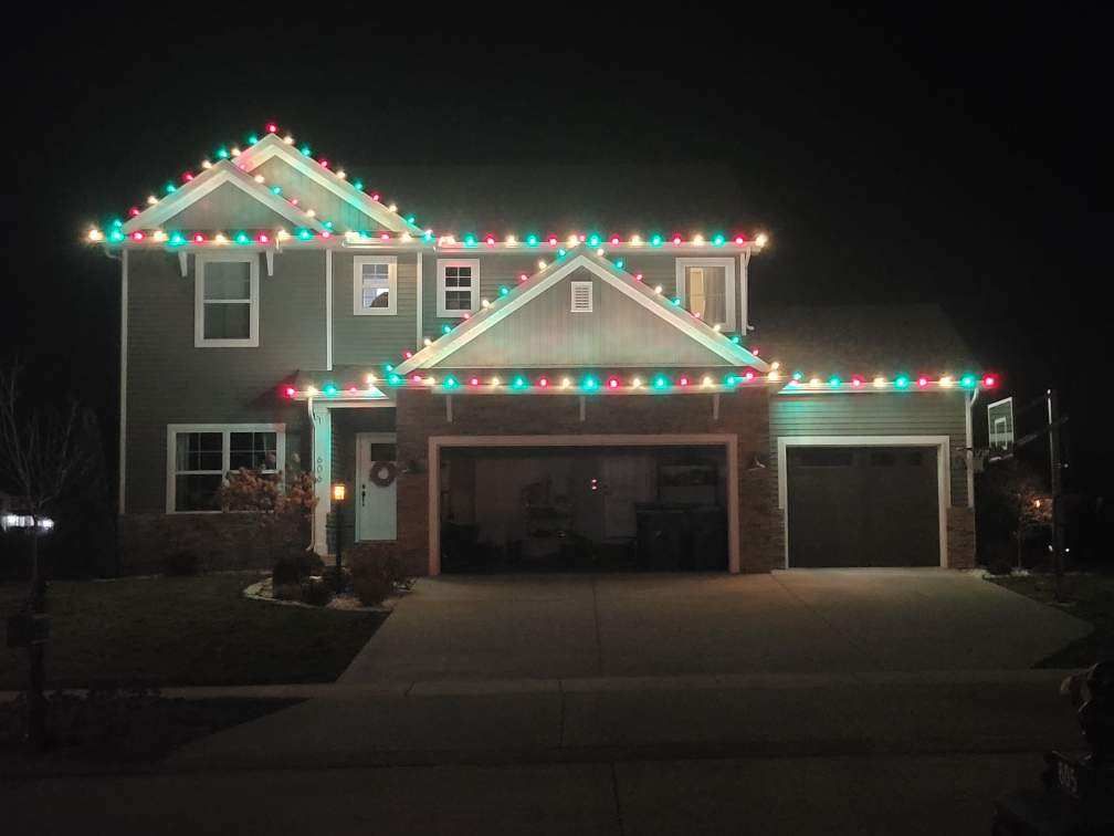 Two-story suburban house at night, outlined with colorful holiday lights and a lit garage.