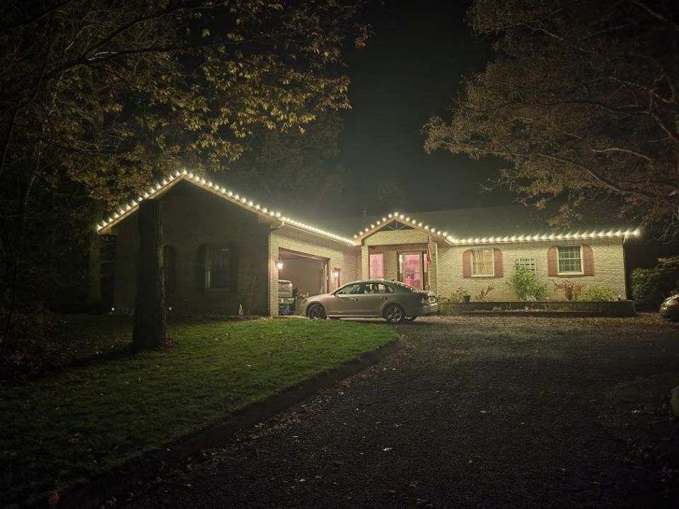 Single-story house lit by white roof lights at night, with a car parked in the driveway.
