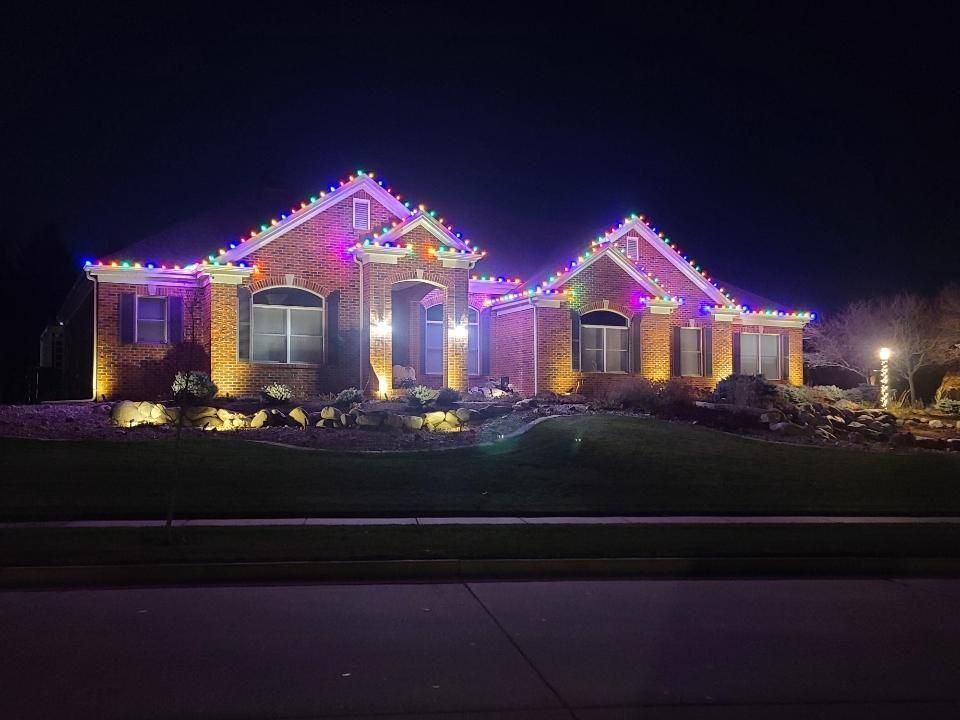 Suburban house at night outlined with colorful Christmas lights and lit landscaping