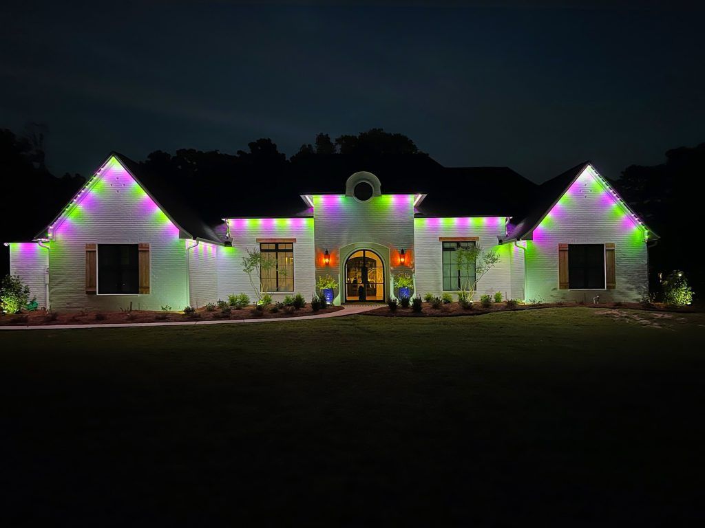 Single-story house at night with colorful purple, green, and white holiday lights along the roofline