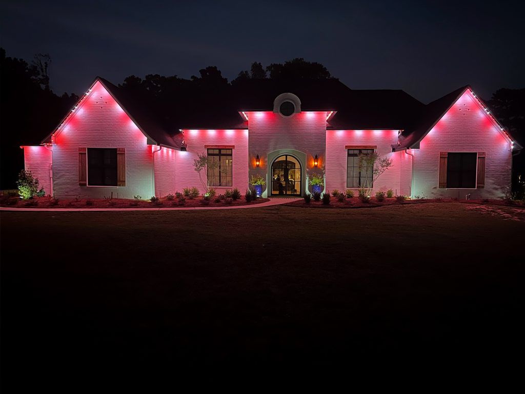 House lit with pink Christmas lights at night, with a decorated front entrance and dark trees behind