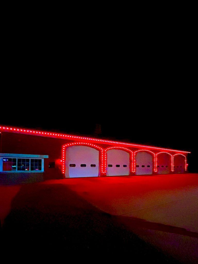 House exterior at night with red holiday lights along the roof and garage arches