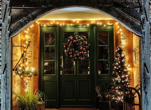 Festive green front door with Christmas wreath, garlands, and warm lights under a stone archway