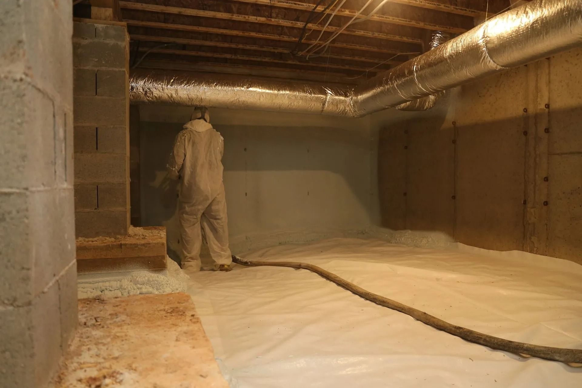 Person in protective suit spraying insulation in a crawl space.