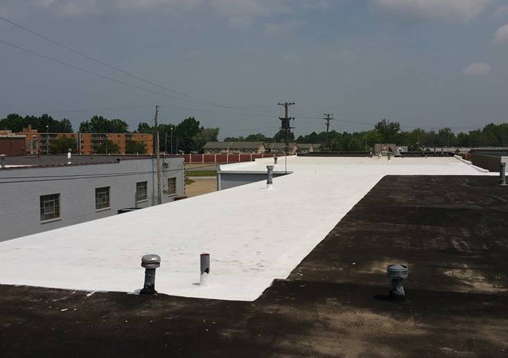 A view of a building rooftop, partially covered in a fresh white reflective coating next to older, dark roofing material.