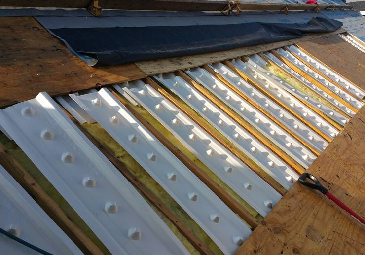 White plastic rafter vents installed between wooden roof trusses under a section of plywood roof decking.