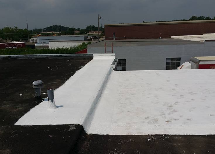 A flat commercial roof features a transition from dark asphalt to a freshly applied white protective sealant coating.