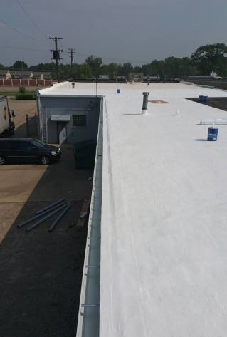 An elevated view of a freshly coated white flat roof on a commercial building next to an asphalt parking lot.