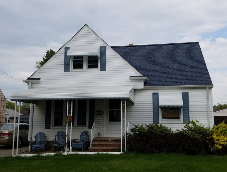 A white one-story house with a blue roof, blue window shutters, and a front porch with three blue chairs.