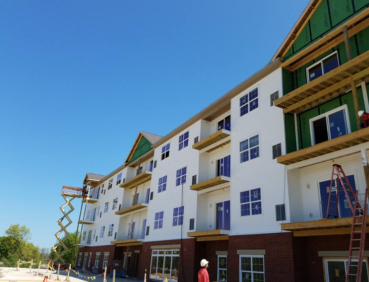Construction workers at a multi-story apartment building under development with brick and white exterior siding.