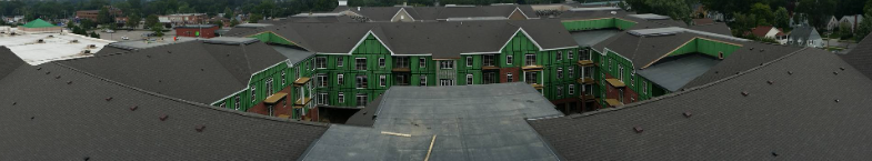 Panoramic view of a multi-story apartment complex under construction with green sheathing and dark shingled roofing.