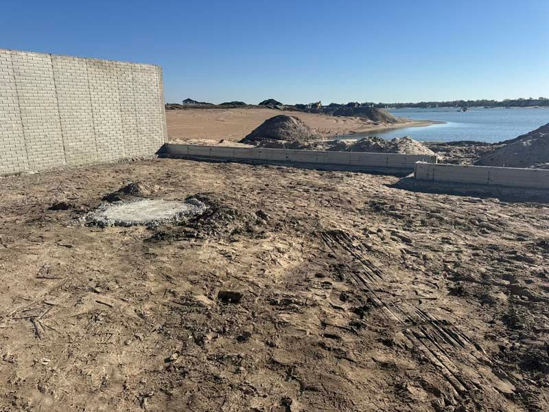 Construction site with concrete wall, dirt, and water in the background.