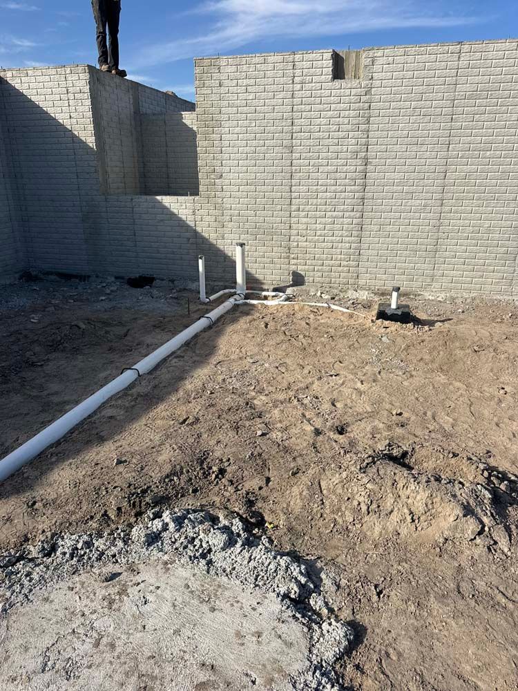 Construction site with white PVC pipes and grey cinder block foundation walls.