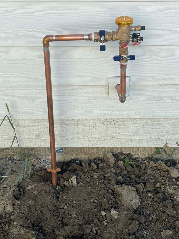 Copper pipe sprinkler system, vertical, against white siding, exposed soil, sprinkler head.