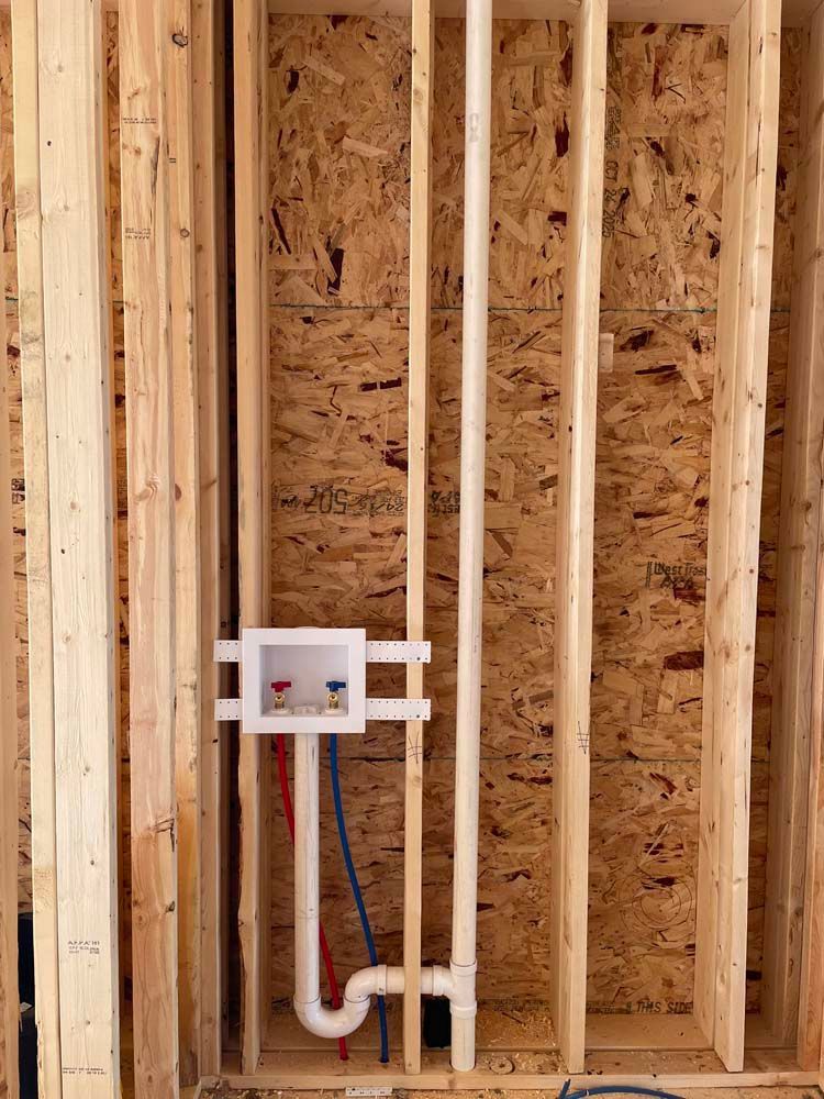 Framing for a laundry room with a white outlet box, pipes, and studs.