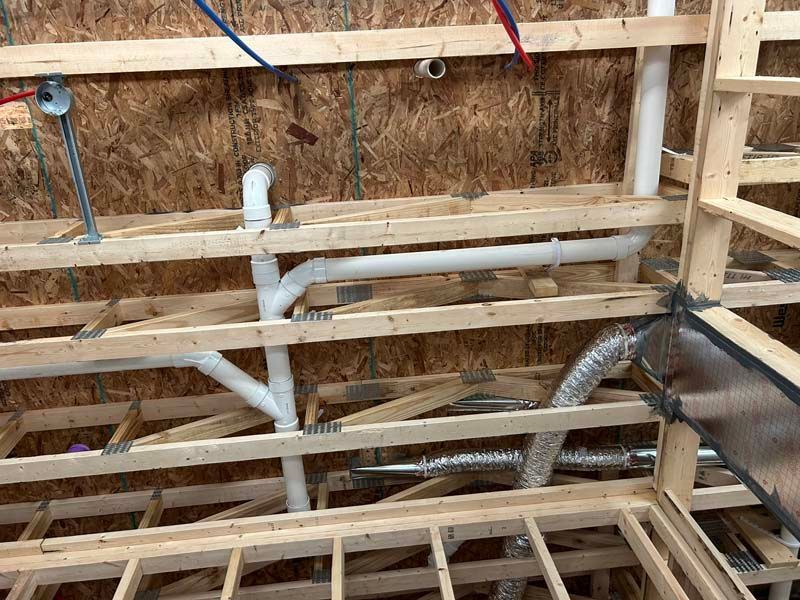 Framed wooden structure with plumbing pipes and ductwork installed.