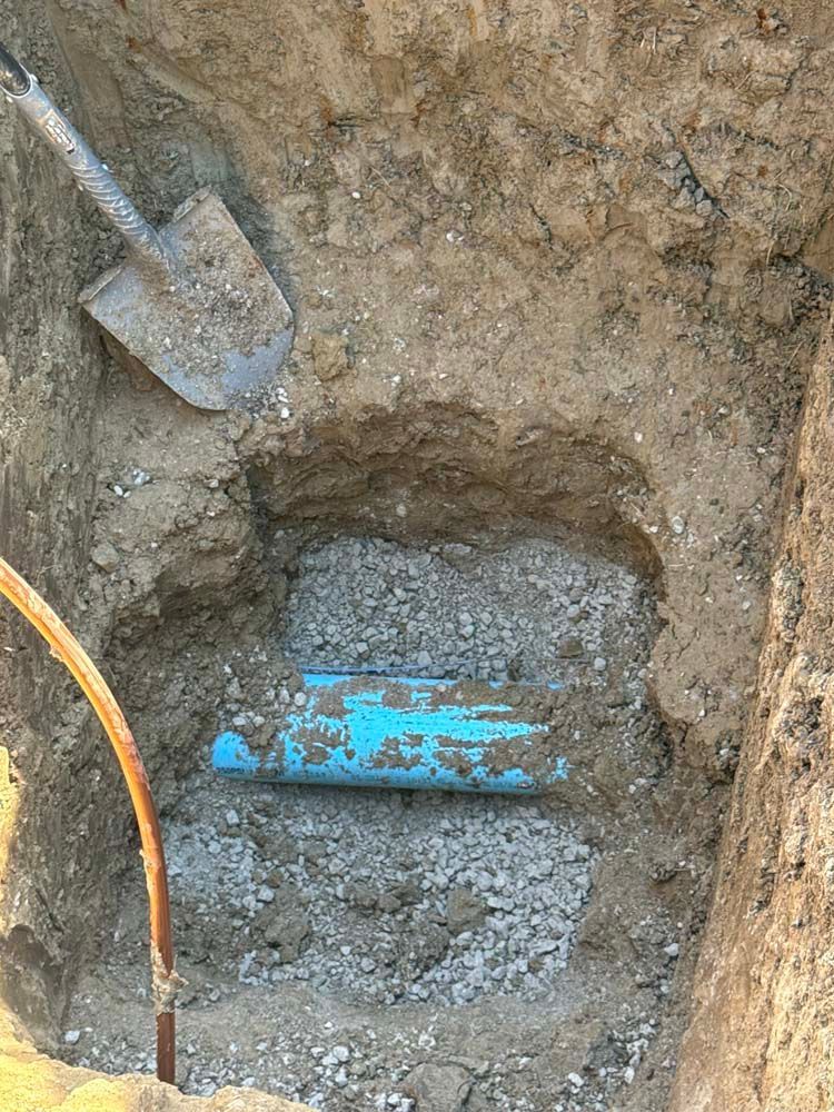 Blue pipe exposed in a dirt hole, shovel rests nearby. Construction site.