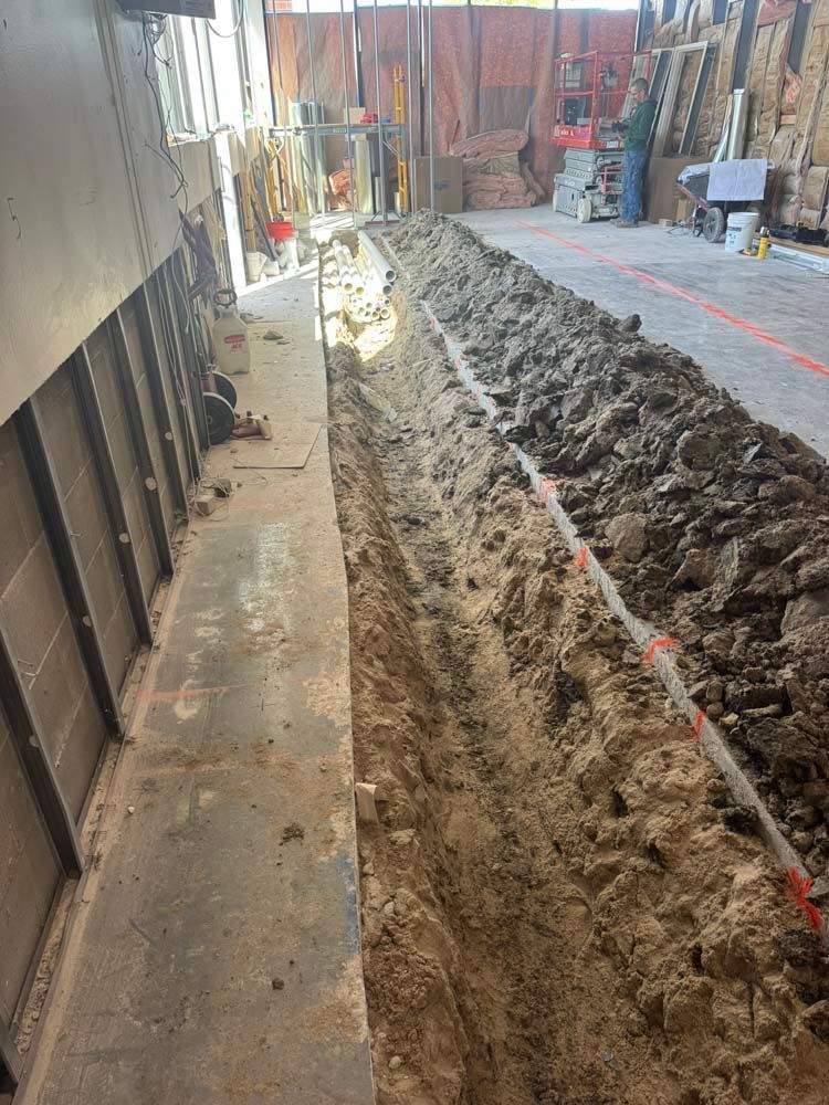 A long trench dug in a concrete floor, with a person standing in the background.