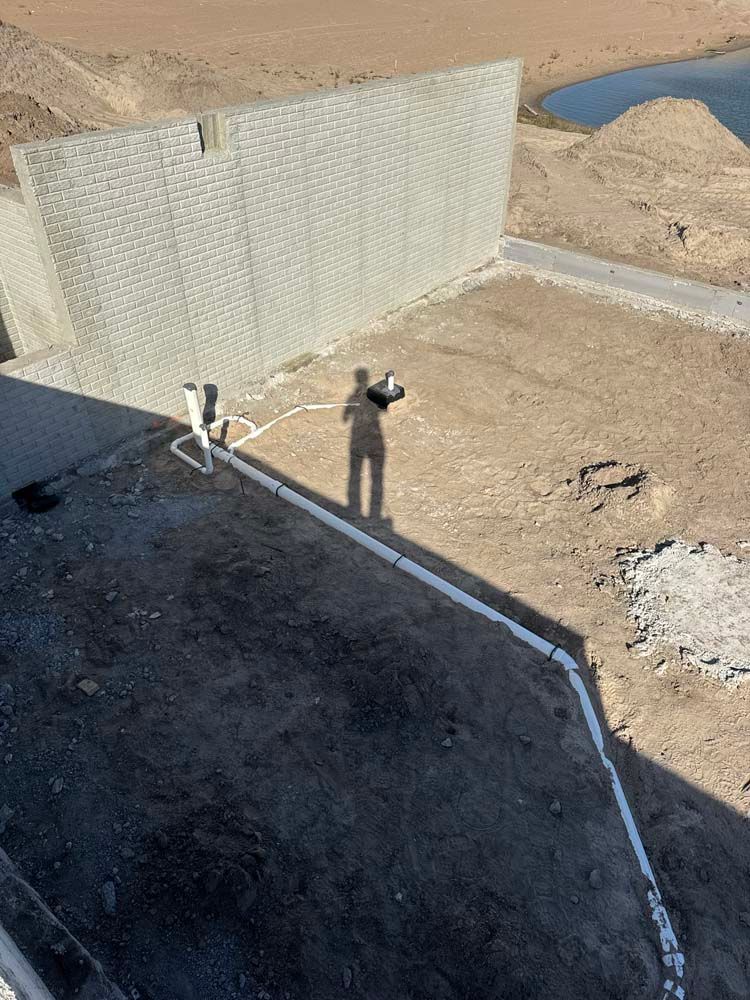 A person stands near a wall, holding a hose, with a body of water in the distance.