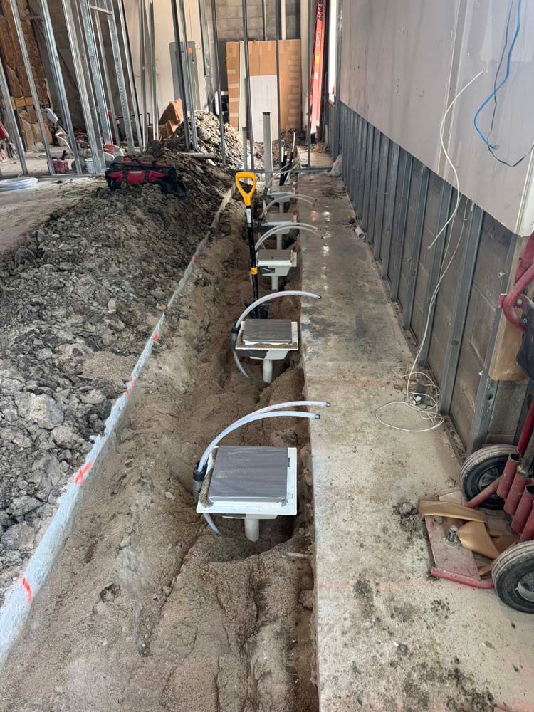A narrow trench with multiple white metal boxes and PVC pipes, likely part of a construction project.