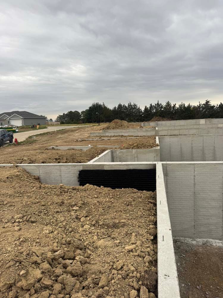 Concrete foundation of a building under construction, dirt pile, cloudy sky.
