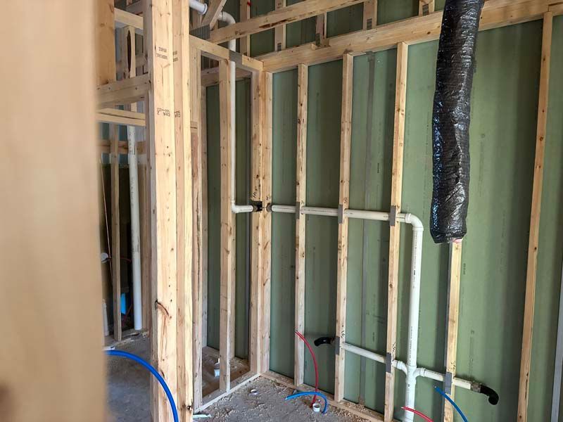 Interior view of a bathroom under construction; wood framing, PVC pipes, and a black duct.