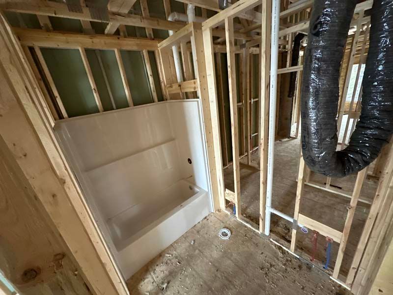 Framed bathroom under construction with a white shower/tub unit installed.
